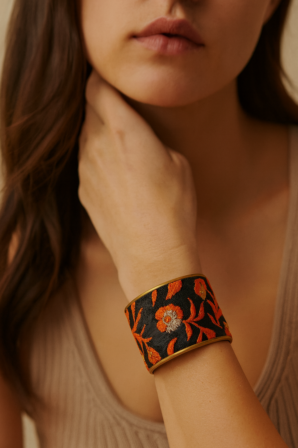 Woman’s wrist wearing the Redd Dott “Shirina” 2″ cuff—black textile with vivid burnt-orange floral and leaf embroidery (gold/silver centers), framed in brushed brass with an open back.