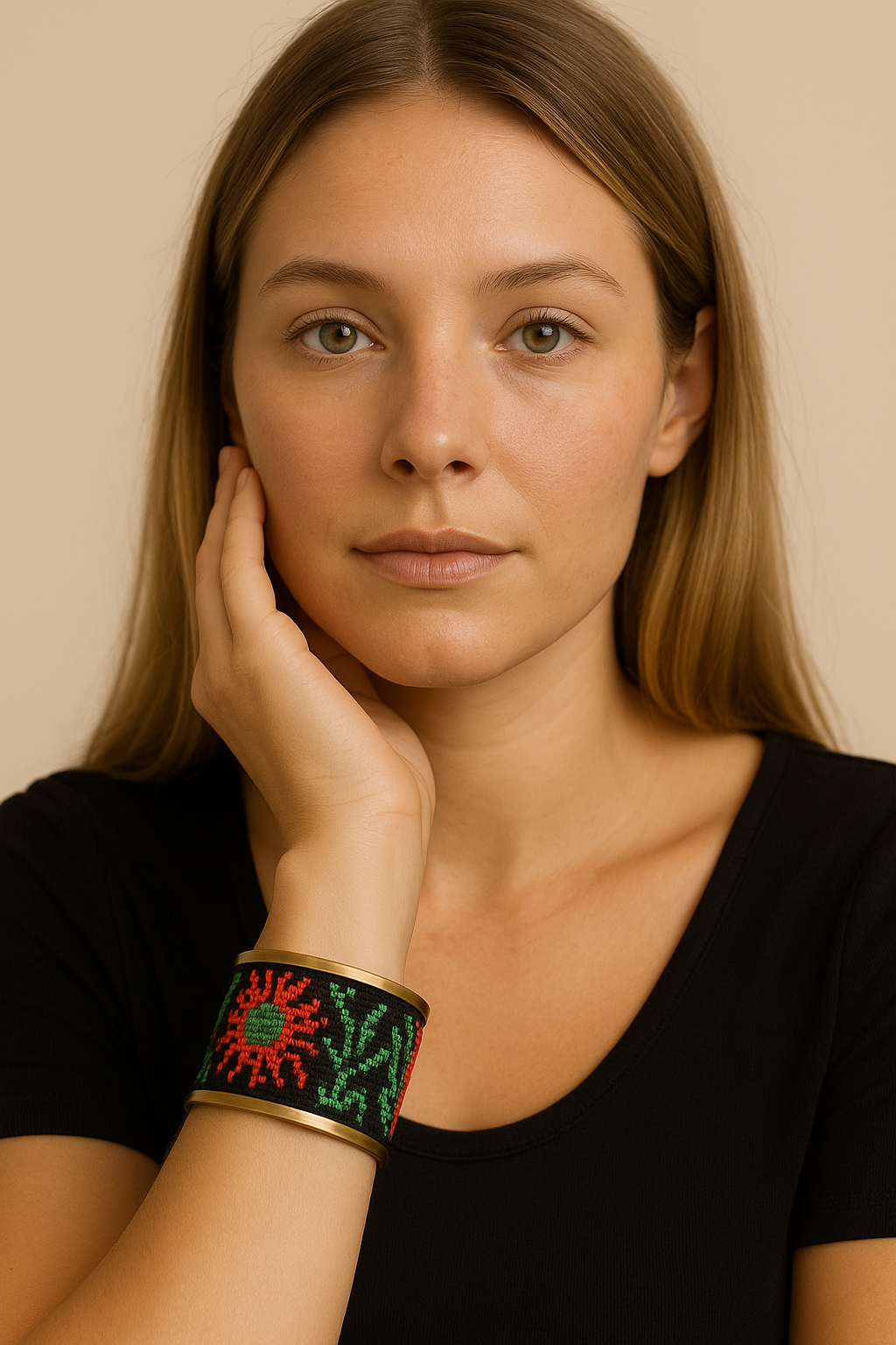 Woman’s wrist wearing the Redd Dott “Shivani” 2″ cuff—black fabric with red-and-green folk cross-stitch sunburst/flower and leafy motifs, framed in brushed brass with an open back.