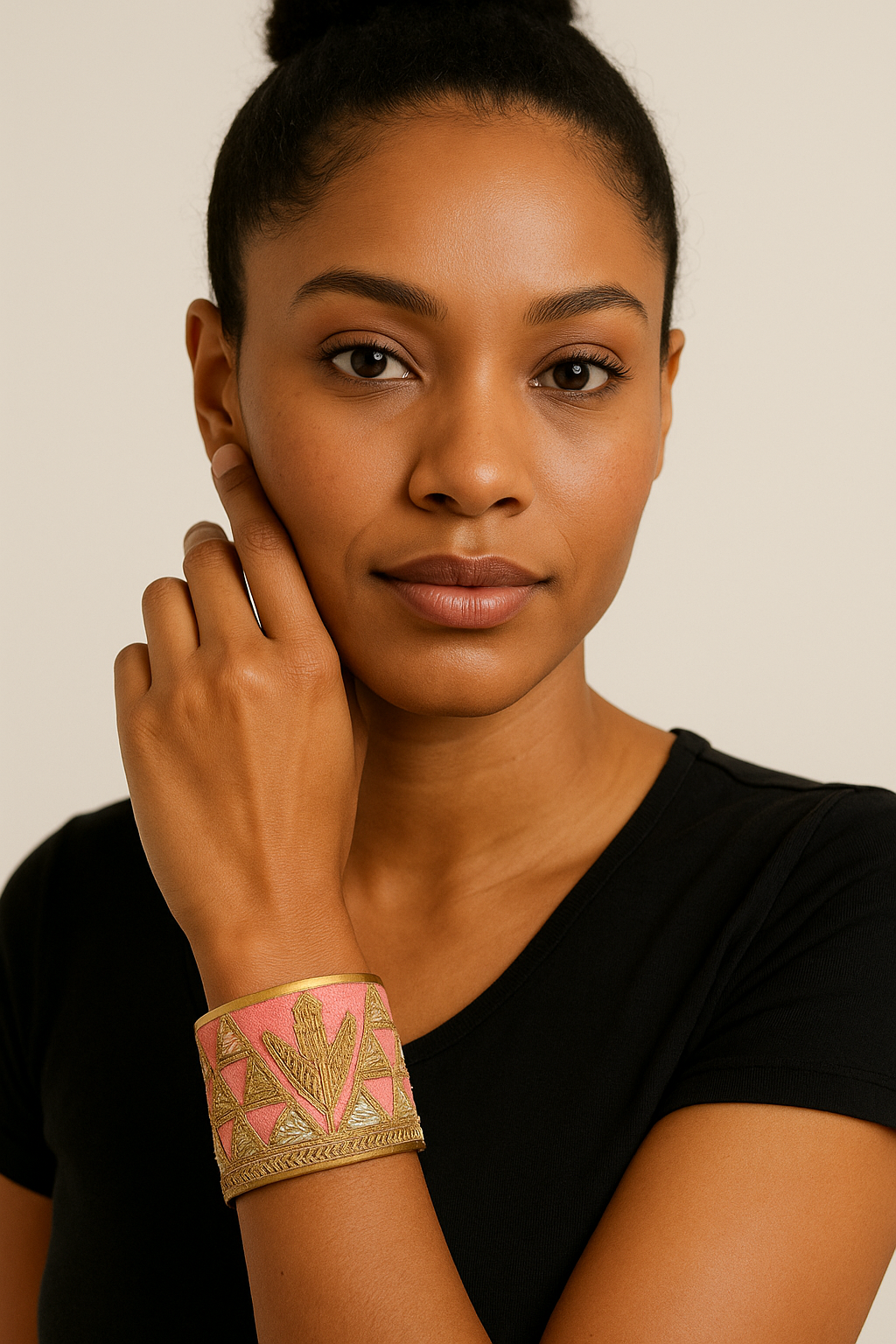 Woman’s wrist wearing the Redd Dott “Sidney” 2″ cuff—blush pink fabric with gold geometric embroidery and a central arrow motif, framed by brushed-brass rims with an open back; styled with a black tee.