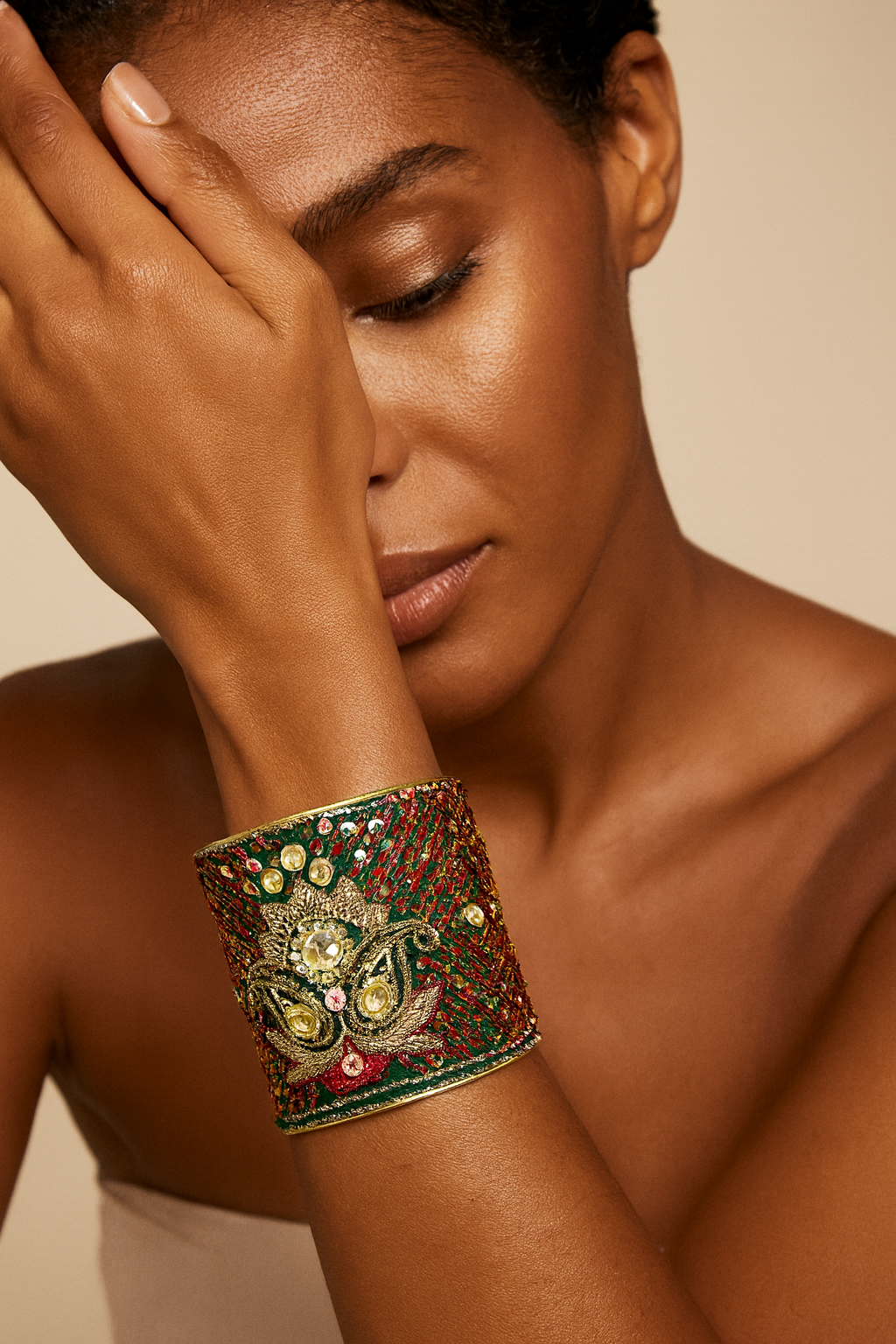 Close-up of a woman wearing the Redd Dott Quinn 3-inch gold cuff bracelet, featuring deep green and red fabric with ornate gold embroidery, sparkling gemstones, and intricate detailing.