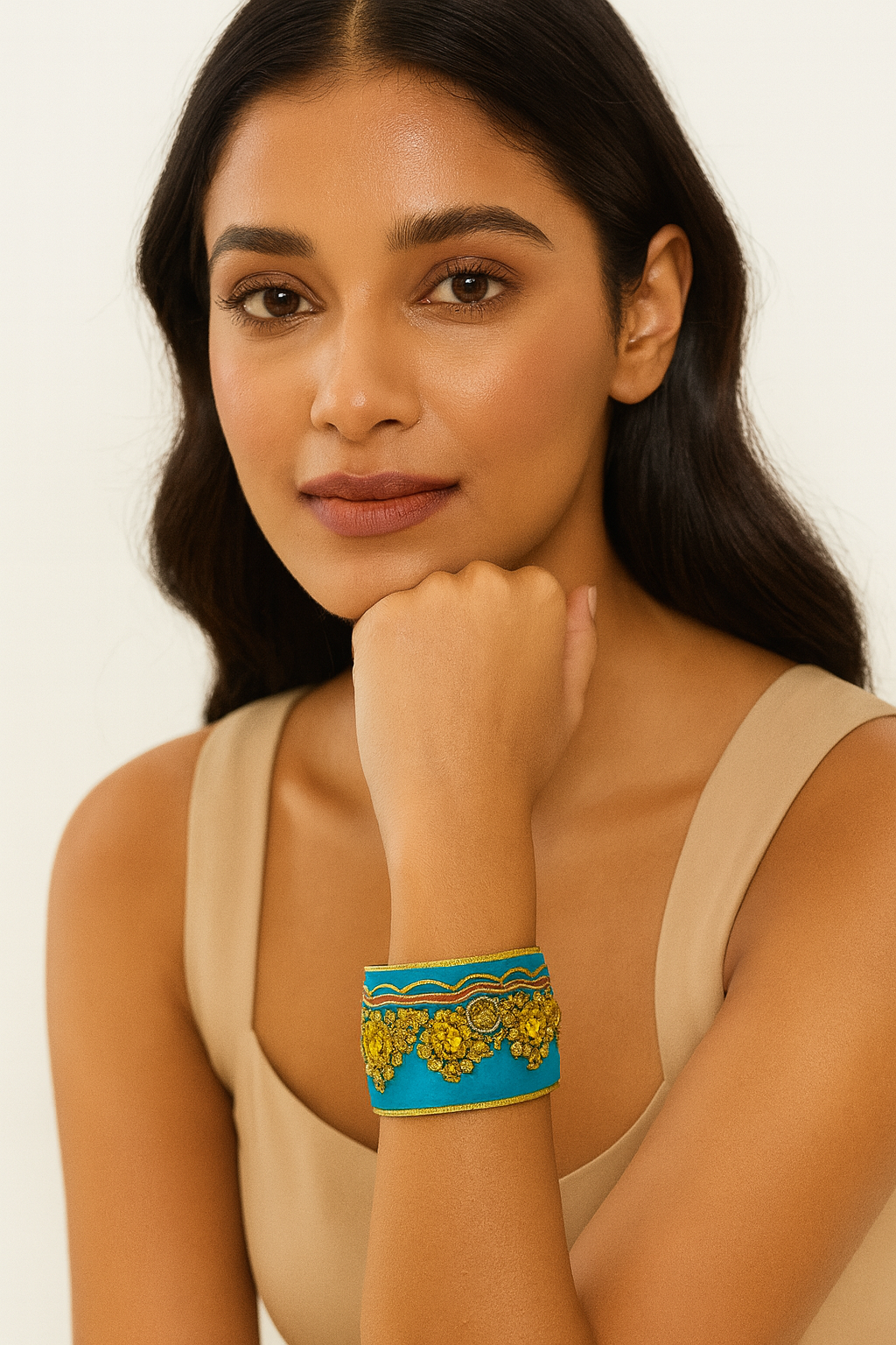 Close-up of a woman’s wrist and lower face, wearing the Redd Dott “Whitley” 2″ wide fabric cuff. The vibrant turquoise cotton is richly embroidered with dense mustard-yellow floral clusters and swirling filigree, topped by scalloped wave-stitch borders in gold and coral, all nestled within a slim open-back brass frame as her hand supports her chin.