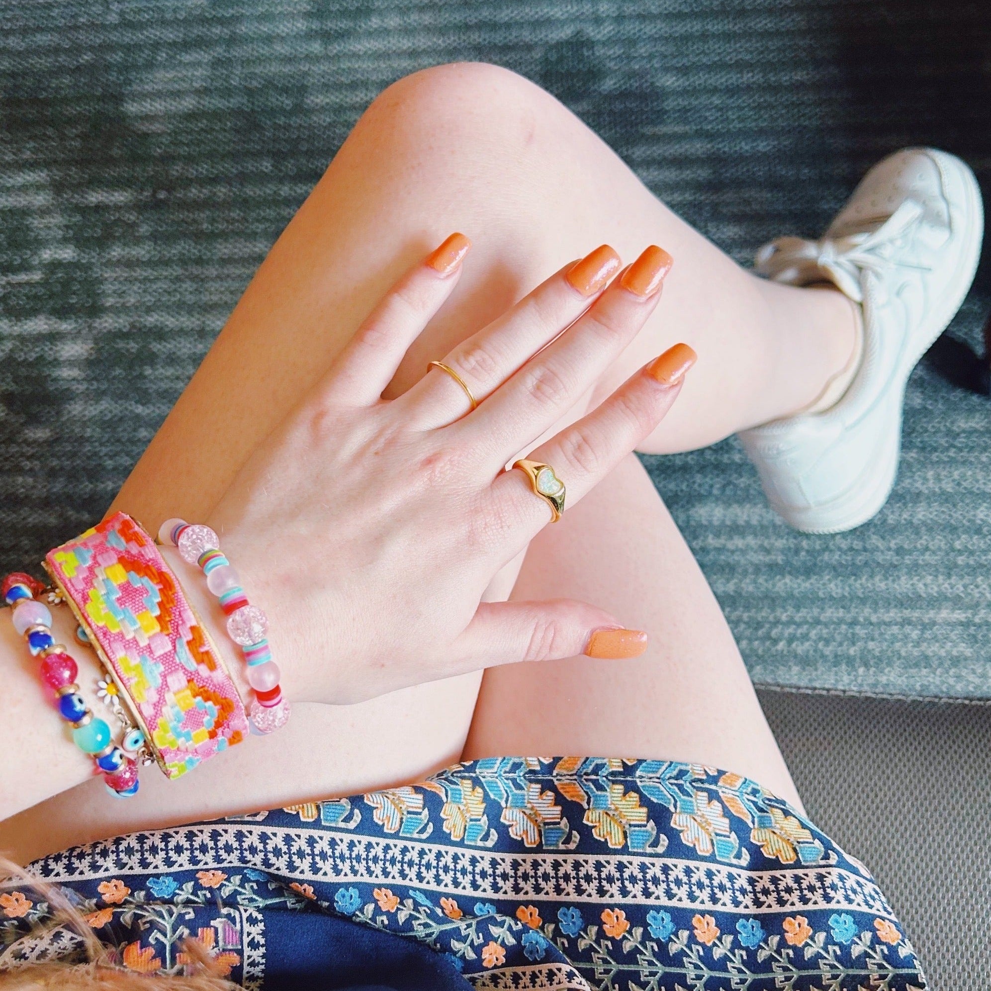 A person wearing the Abigail brass cuff bracelet along with beaded bracelets and gold rings, showing off the embroidered pink and neon geometric design in a playful, casual summer outfit—vivid and meaningful inspirational jewelry.