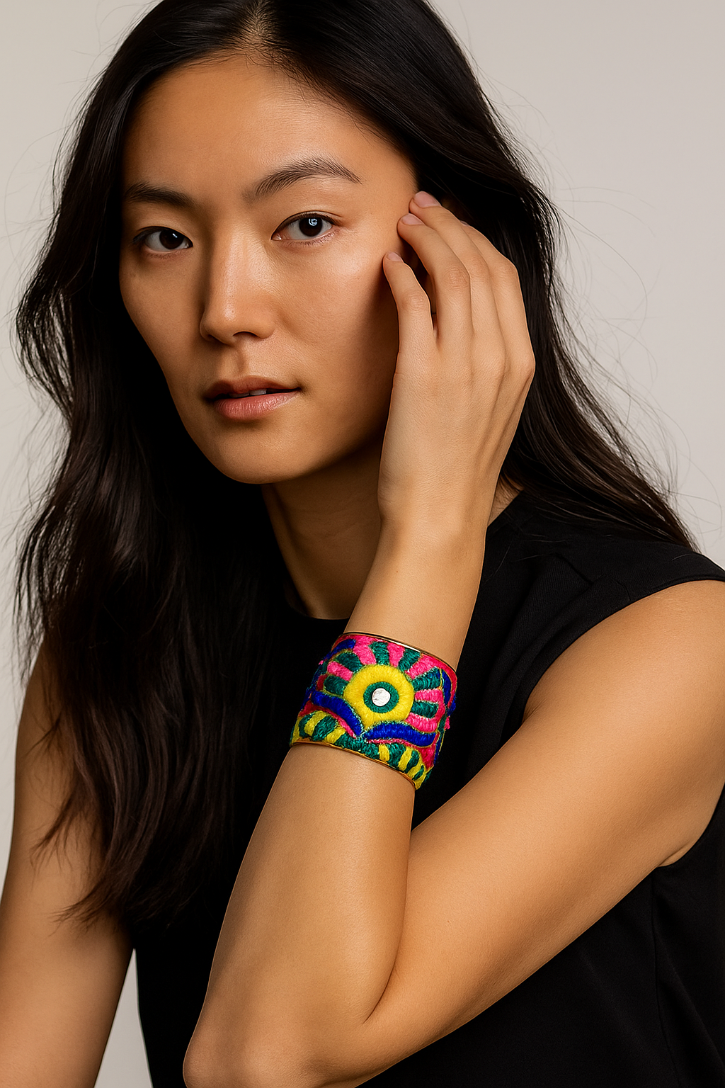 Close-up portrait of a female model wearing a 2-inch wide scarlet hand-embroidered brass cuff bracelet; the open-back ends peek out as she gently touches her hair.