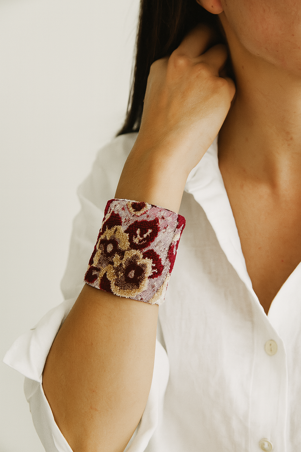  woman’s arm wearing a wide 3-inch brass cuff bracelet featuring deep red and golden velvet floral patterns on fabric, exuding the warmth and passion of nature inspired jewelry and inspirational jewelry.