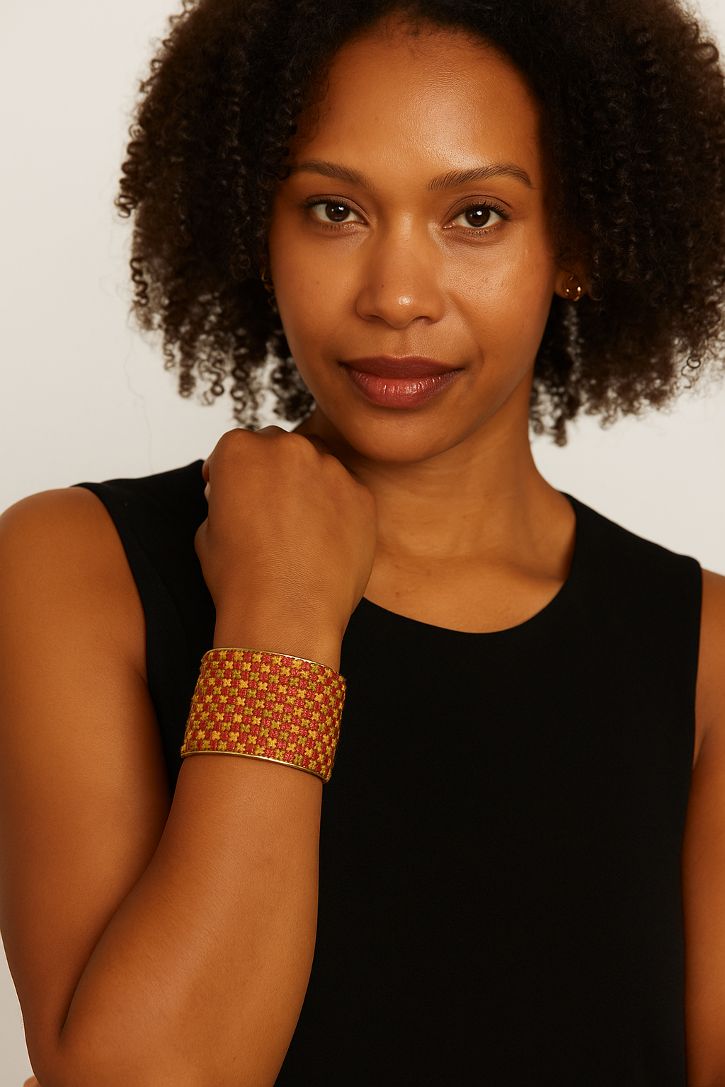 A female model wears a three-inch brass cuff bracelet wrapped in olive, yellow, and pink mosaic-check embroidered fabric; 
