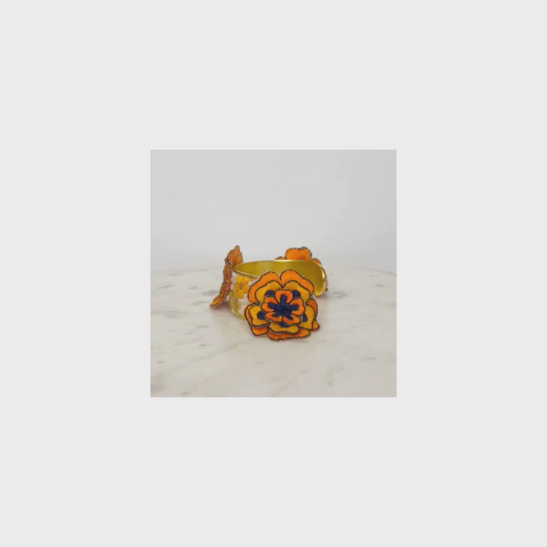 A yellow flower cuff bracelet with an orange and black floral design displayed on a white marble surface.