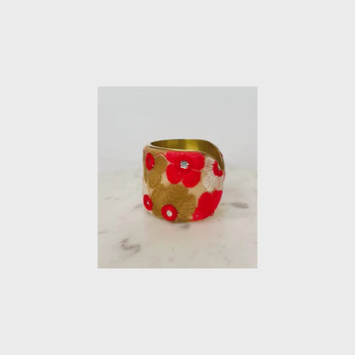 A vintage brass cuff embroidered bracelet with handwoven flowers in cream, red and gold with mirrored center accents sits atop a white marble surface.