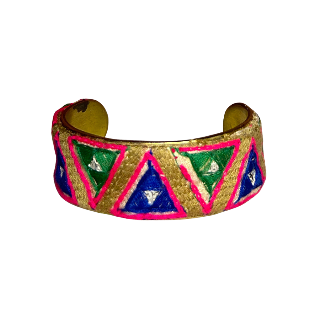 The Tabitha brass cuff bracelet features vibrant embroidered triangles in green, blue, pink, and gold. This bold geometric bracelet is a true power piece, crafted on a vintage-style brass base for maximum impact.