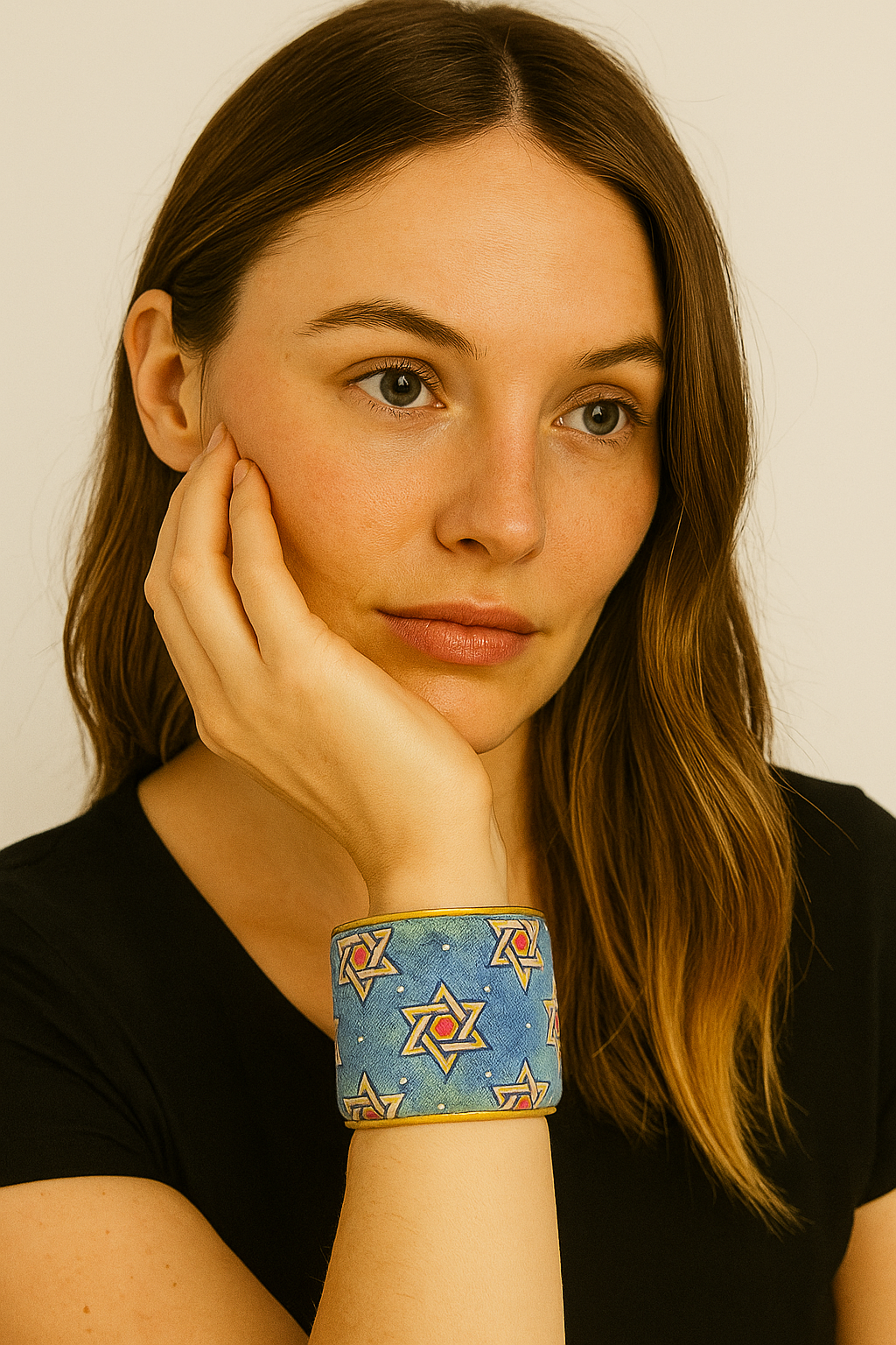 A woman wearing a 2-inch wide brass cuff bracelet wrapped in celestial blue fabric with repeating gold six-pointed stars and red centers. She rests her chin in her hand, showcasing the cuff’s color and pattern beautifully.